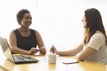 Two young women talking in an office.