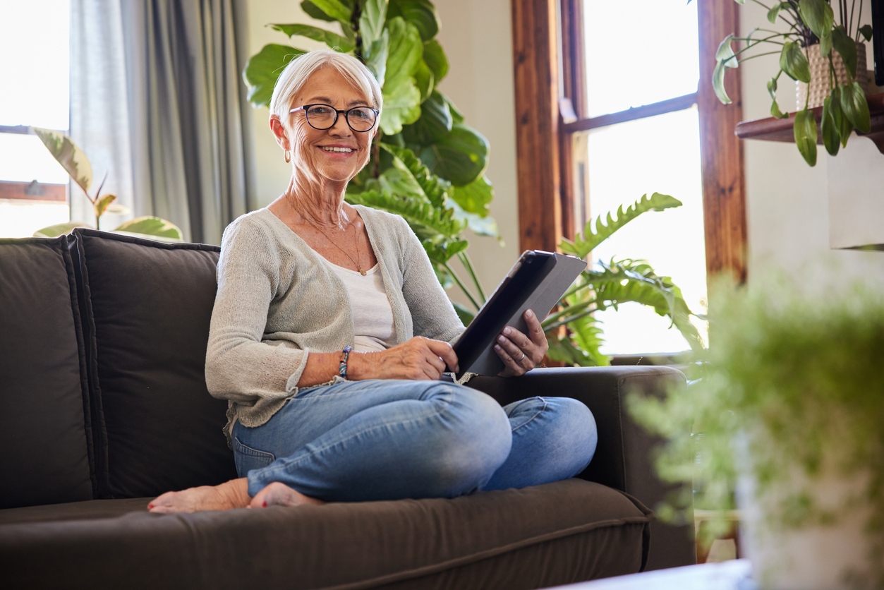 Smiling senior woman using a digital tablet on her living room sofa