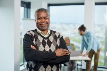 A smiling multicultural senior student is standing with arms crossed in a classroom and looking at the camera. Seniors with bachelor's degree concept.